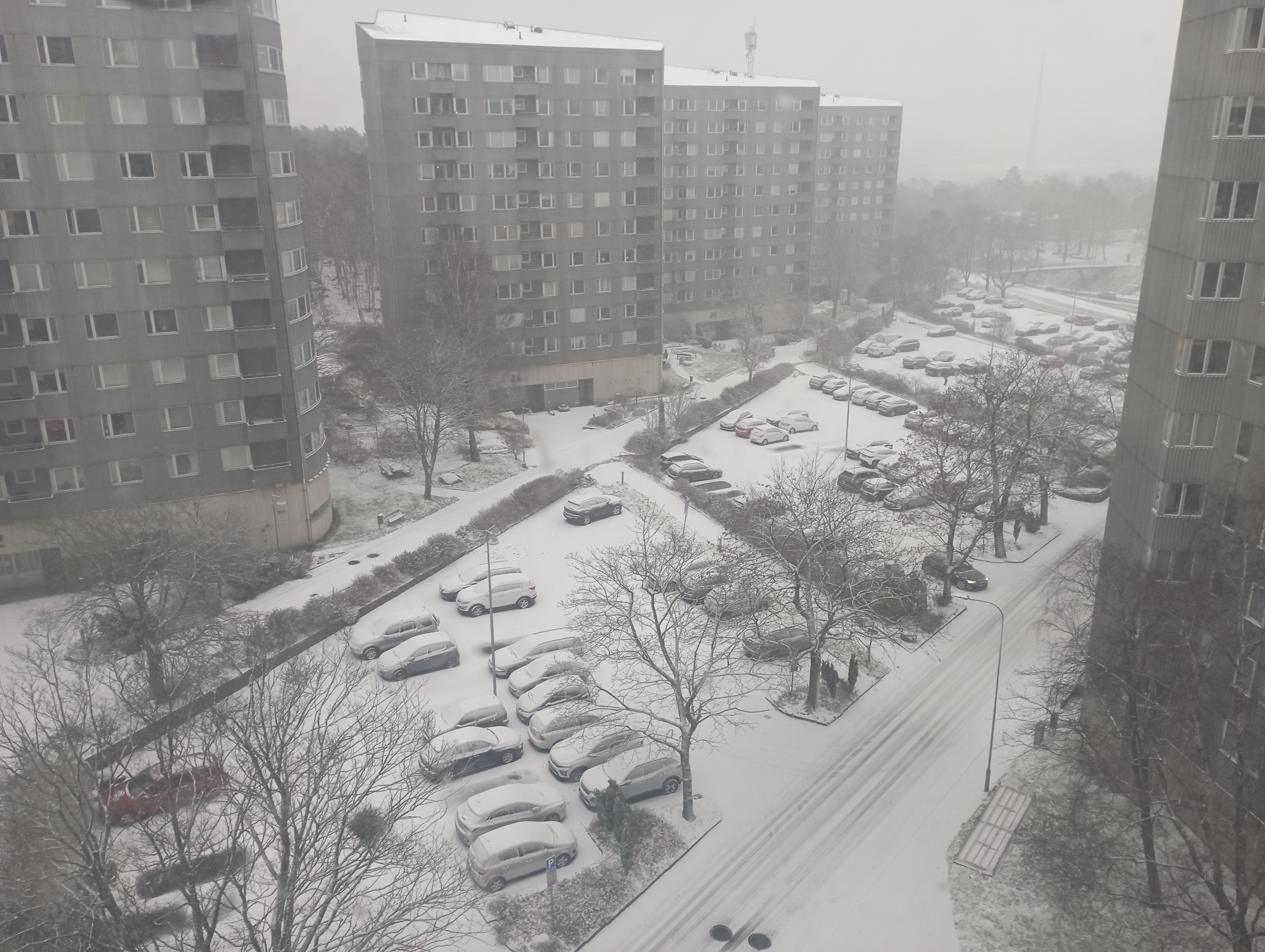 View looking out over apartment buildings and a parking lot, all covered in a little bit of snow
